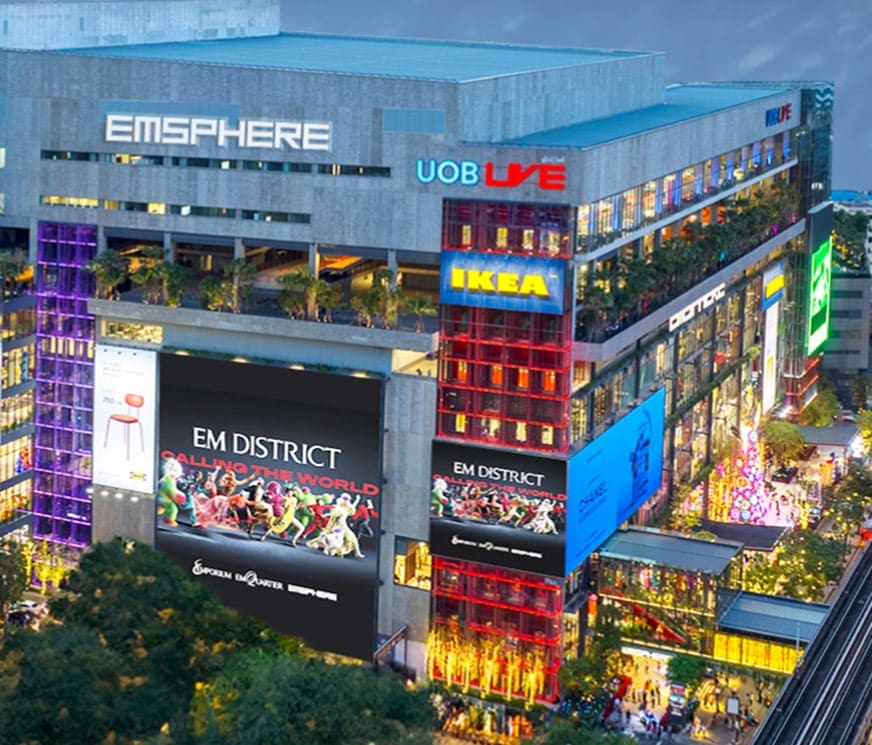 The EmSphere at dusk, a grey block with EmSphere, UOB Live and IKEA signs and large EM District billboards