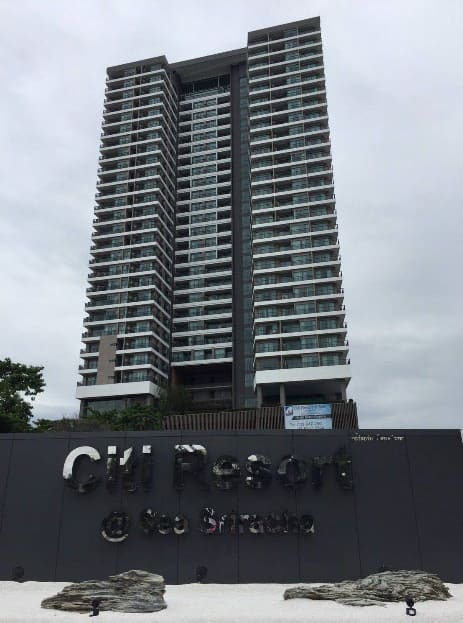 Citi Resort Sriracha, a grey residential tower on an overcast day behind a dark sign wall bearing the development's name