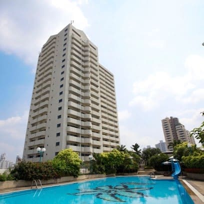 A serviced-apartment tower rising behind a swimming pool with a mosaic floor, a blue water slide and planting