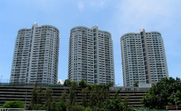 Three curved white residential towers rising above a multi-storey car park and trees under a blue sky