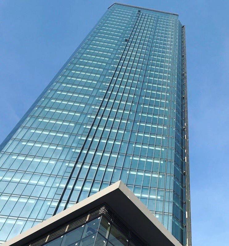 MS Siam Tower, a tall glass office tower seen from directly below against a blue sky, above a glazed podium corner
