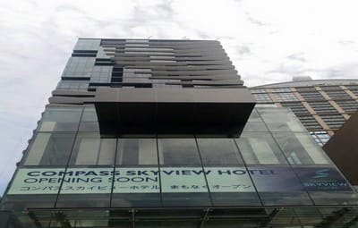 Looking up at the glass Compass SkyView Hotel tower with an "opening soon" banner above the entrance