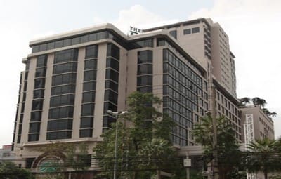 The Emerald Hotel on Ratchada Road: a beige high-rise with dark glazing behind street trees and power lines