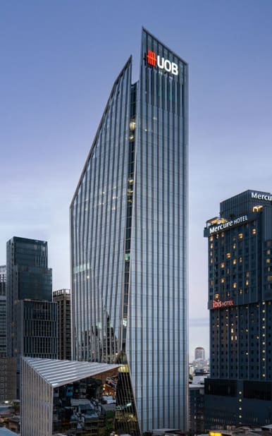 UOB Head Office, a slender glass tower with an angled crown, photographed at dusk beside a hotel tower