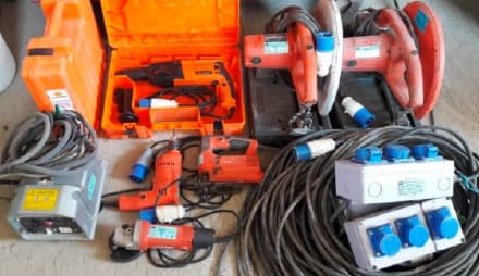 Power tools laid out on a floor for inspection: rotary hammer, cut-off saws, jigsaw, drill, grinder, cables and socket boxes