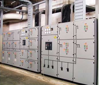 Grey motor-control and distribution panels with coloured indicator lamps, below cable trays and insulated ducts