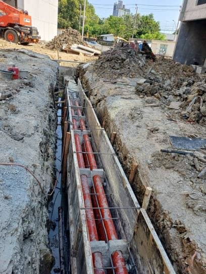 Trench lined with timber formwork holding red cable conduits on spacers with rebar ties, with spoil heaps and a mobile crane beyond