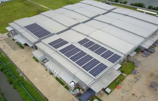 Aerial view of a large factory with several solar panel arrays on its stepped metal roofs