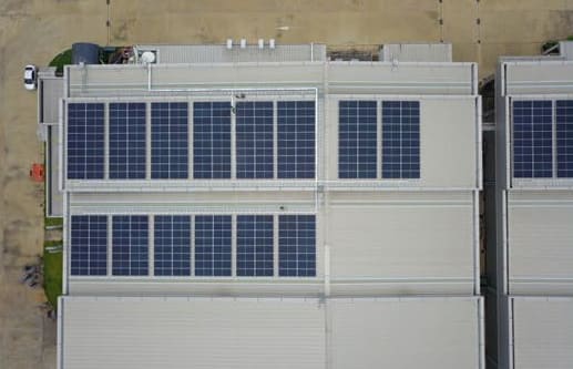 Top-down aerial view of factory roofs with rows of solar panels