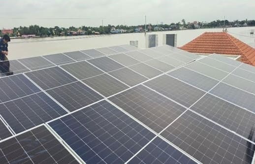Rows of installed solar panels on a flat roof beside an orange tiled roof, with a river beyond