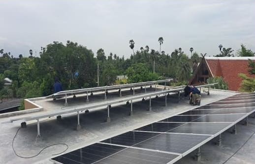 Workers fixing aluminium mounting rails on a flat roof, with a row of solar panels already installed in front