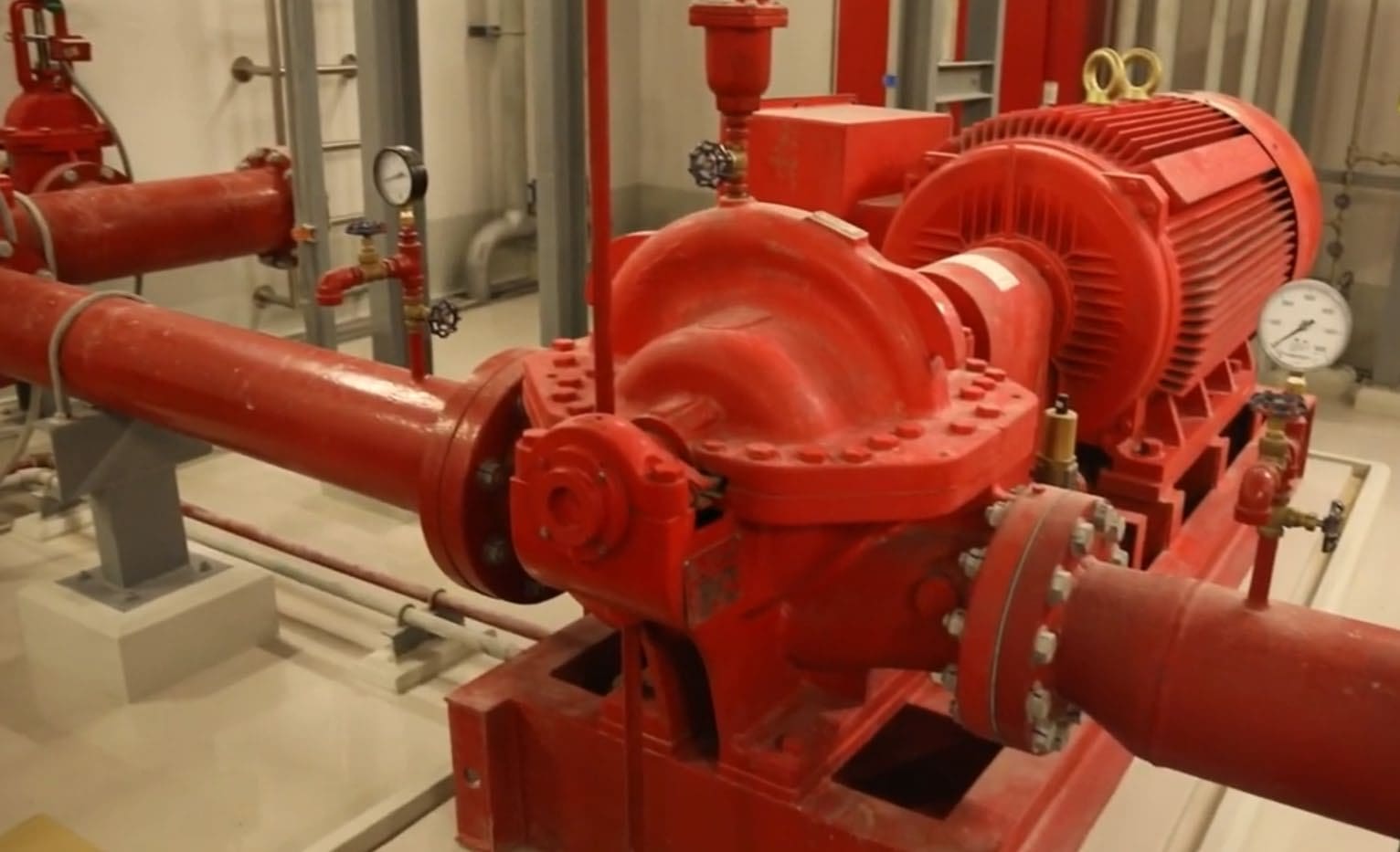 Red horizontal split-case fire pump and motor on a steel base, with pressure gauges and red pipework