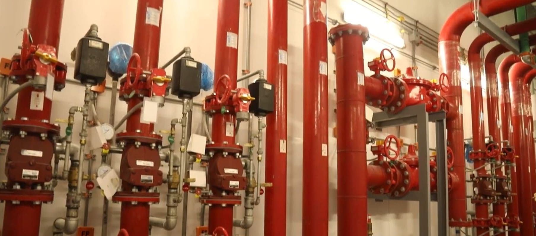 Row of red fire-protection risers with alarm valves, gauges and handwheel valves along a pale wall