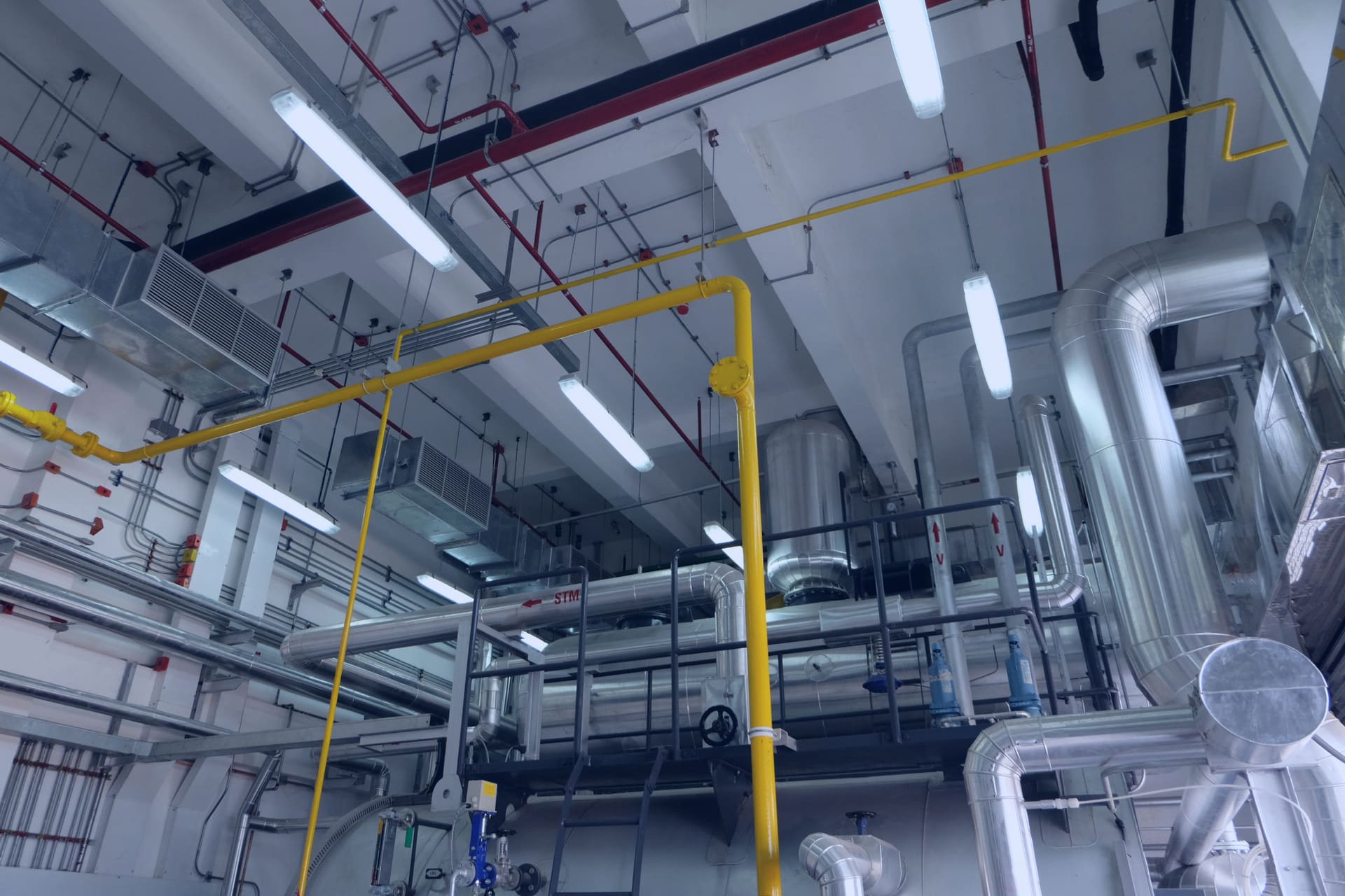 Boiler room with a large insulated boiler shell, a railed catwalk and aluminium-clad steam pipes under overhead ducts