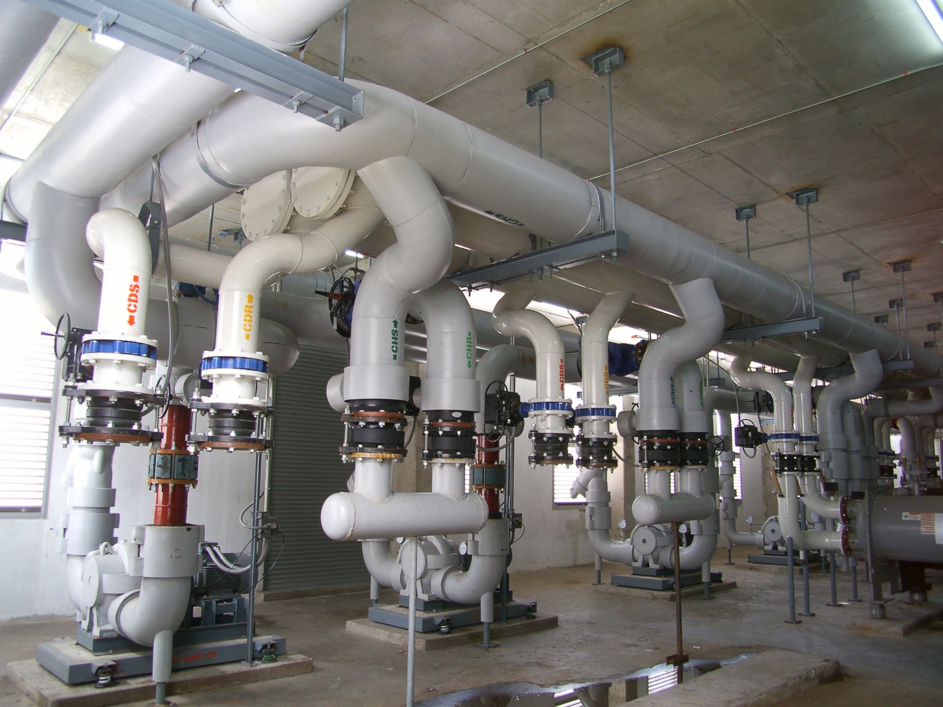Chiller plant room with white insulated pipes labelled CHS, CHR, CDS and CDR rising from a row of pumps