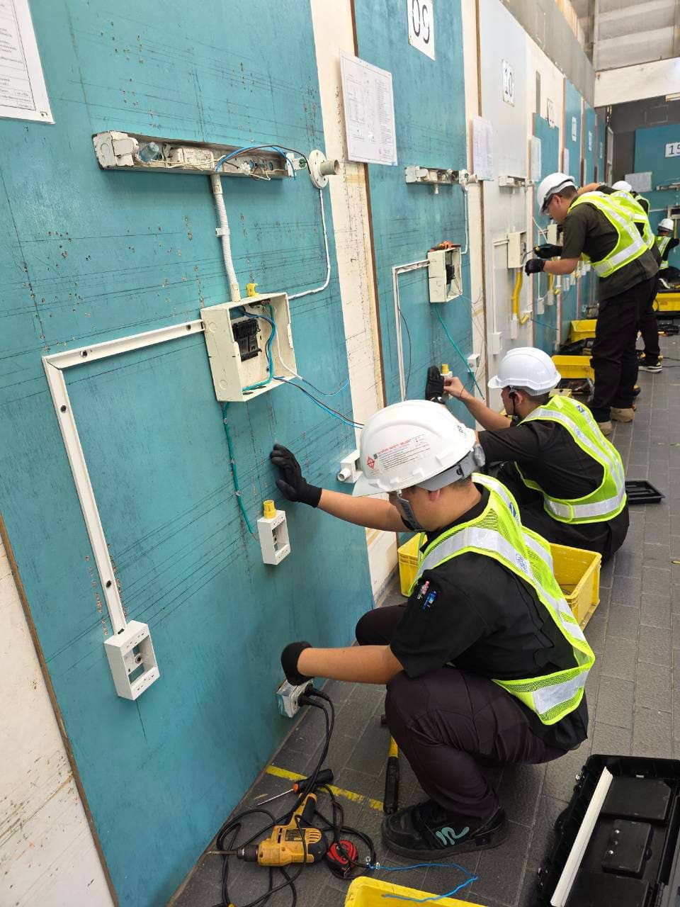 Test candidates in hard hats and hi-vis vests wiring test boards during a skill test
